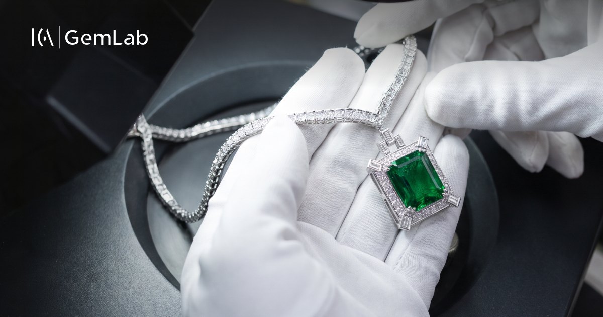 An emerald and diamond pendant held in gloved hands at ICA | GemLab